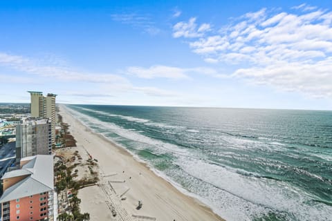 Stunning aerial view showcases the pristine coastline with wide sandy beaches, rolling surf, and high-rise beachfront development extending along the shore.