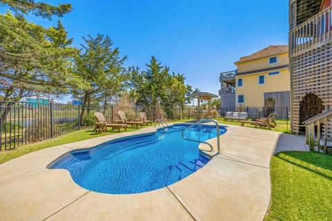 A sparkling private pool surrounded by lounge chairs and lush greenery, perfect for sunny days. The fenced yard offers space to relax while glimpses of blue water peek through the trees beyond.