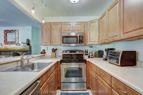 A modern kitchen with stainless steel appliances, light wood cabinets, a double sink, and small appliances like a toaster oven and coffee maker on the countertops.