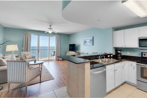 Your oceanfront condo flows seamlessly from kitchen to living area, with stunning sea views through floor-to-ceiling windows creating the perfect coastal retreat.