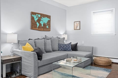 Bright and cozy living room with a plush sectional sofa, modern glass coffee table, and stylish world map wall art — the perfect space to relax, unwind, and gather with family after a day of exploring.