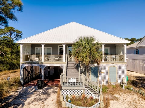 Coastal cottage with covered porch featuring tropical landscaping and nearby beach access in a peaceful residential setting.
