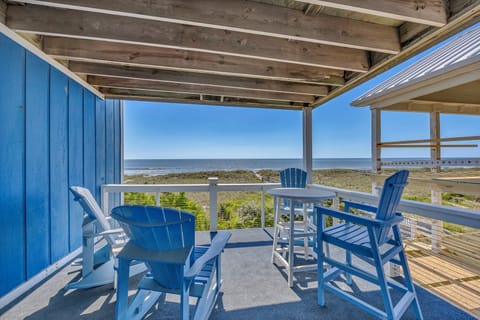 Coastal property featuring covered deck seating and oceanfront access across dune vegetation.