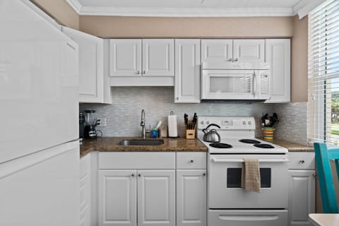 Fully equipped kitchen with fridge, oven, stove, microwave, and Keurig coffee maker, flowing into a cozy living and dining space.