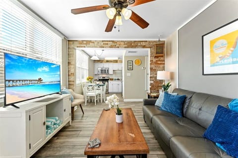 Living room area with a sofa bed, 2 single chairs, smart TV, and ceiling fan.