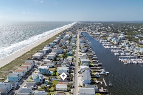 Aerial view of a coastal community featuring pristine beaches, marina with boats, and residential properties nestled between ocean and waterway.