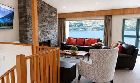 Open-plan living with gorgeous lake and mountain views, a striking stone feature wall with electric fireplace, and bifold doors opening onto a private balcony and deck.