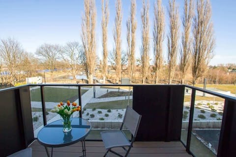 A balcony with a chic outdoor seating arrangement, providing views of a landscaped garden and tall poplar trees, ideal for relaxing with a morning coffee or evening drink.