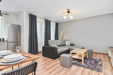  A modern living room with a gray sofa, wooden coffee table, TV, and large windows with sheer curtains.