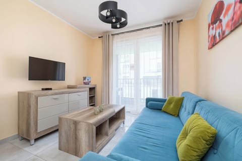  A living room with a blue sofa, TV and bright curtains. The space is lit with natural light from large windows.

