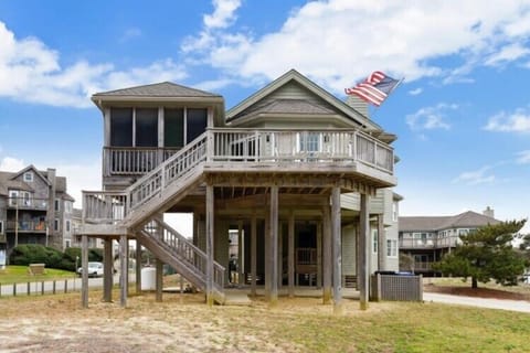 Coastal vacation home elevated on stilts, featuring screened porch and upper deck with American flag. Located in a quiet residential beach community.