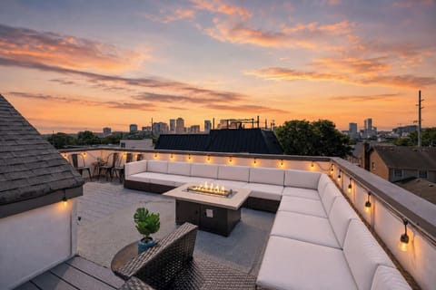 Cozy up around the firepit on this stylish rooftop with wraparound sectional seating - Panoramic city views under cotton candy skies create a magical evening atmosphere - String lights, stylish furnishings, & skyline charm set the perfect sunset scene