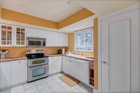 - Fully equipped kitchen with double oven, microwave, and ample counter space
- White cabinetry and tiled floors pop against a golden accent wall for warmth
- Window over the sink brings in sunlight and a cozy home style feel