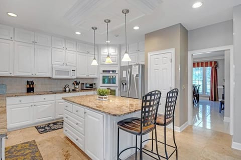 - Warm pendant lighting highlights the large island perfect for serving or casual bites
- Double ovens, stainless fridge, and tall cabinets offer full hosting flexibility
- Walkway leads directly into dining space for effortless food flow