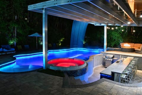 Luxury backyard with blue-lit swim-up bar pool, waterfall feature, round hot tub and outdoor lounge area, Orlando Florida