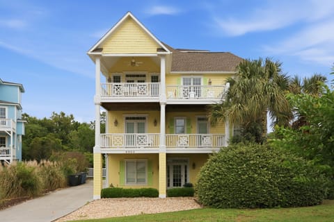 Charming three-story coastal property featuring multiple private balconies, surrounded by lush landscaping and tropical palms in a peaceful residential setting near the beach.