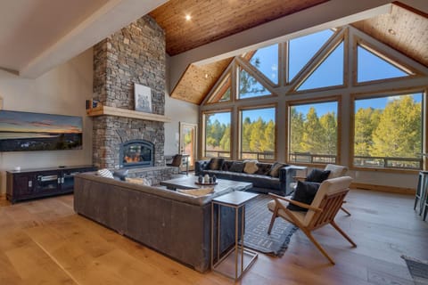 - Open concept living area with floor to ceiling forest views  
- Stunning stone fireplace centerpiece adds cozy cabin charm  
- Spacious layout with modern seating and natural light