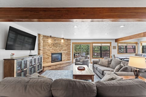 Unwind in your spacious living area with cozy sectional seating, warm stone fireplace, and modern entertainment center for perfect relaxation.