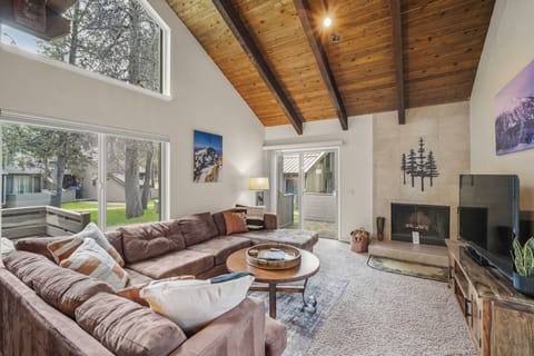 Sink into plush seating beneath soaring wood-beamed ceilings, where natural light streams through tall windows framing peaceful tree views. Gather by the cozy fireplace for memorable mountain evenings.
