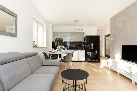 A living room with a TV, a dining table, and large windows providing natural light.
