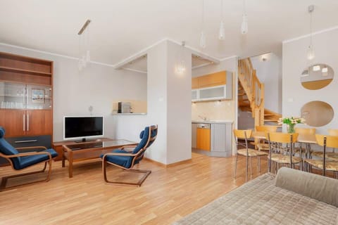 A bright living room with large windows, wooden flooring, and cozy furniture, including a modern sofa and armchairs. The room has a spacious, open feel and stylish decor.