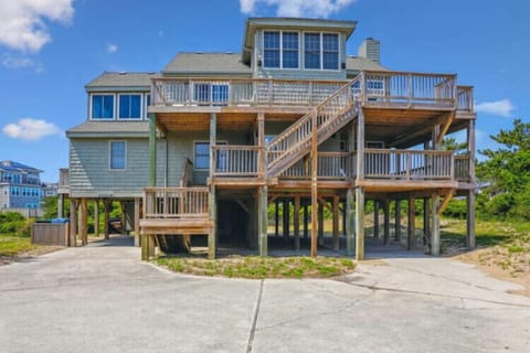 Elevated beachfront property featuring multiple deck levels and spacious outdoor living areas, with neighboring homes visible and coastal vegetation in the surrounding area.