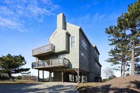 Coastal vacation home elevated on sturdy pilings with wraparound decks offering elevated views of the surrounding landscape and blue skies.