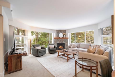 - Bright living room with mountain views through tall glass - Gather by the warm stone fireplace after skiing or hiking the Whistler trails - Plush seating and natural light create a cozy alpine-inspired retreat for all