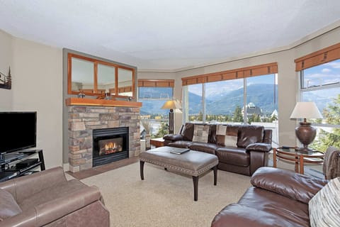 - Warm living room with panoramic mountain views through wide windows  
- Stone fireplace adds a cozy alpine touch for après-ski relaxation moments  
- Spacious seating perfect for gatherings after a day on the slopes  
