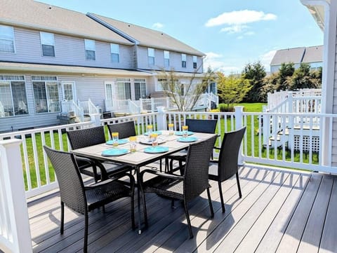 618 Driftwood Court - Sun-Drenched Outdoor Entertainment Space - This spacious wooden deck is furnished with a large dining set, perfect for enjoying meals in the coastal air. White railings surround the area, offering a safe and private space with views of the lush community grounds.