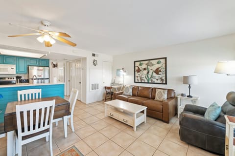 Unwind in your open-concept living space with comfortable leather seating, coastal-inspired kitchen, and ceiling fan for perfect relaxation.