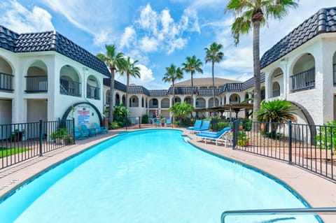 Property features Mediterranean-style architecture with blue tile roofs surrounding a central swimming pool area with tropical palm trees.