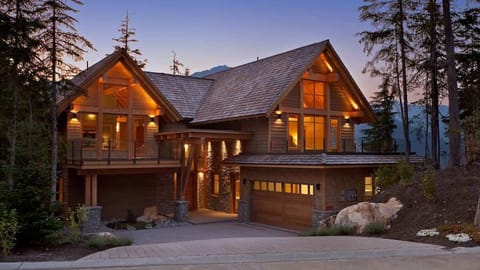 - Modern chalet exterior glowing warmly at sunset among trees  
- Large windows showcase cozy interiors and inviting design  
- Peaceful mountain setting ideal for relaxing evenings away  
