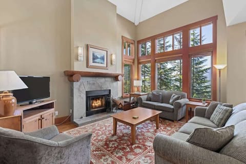 - Inviting living room with stone fireplace and tall windows framing pine forest views  
- Plush seating and warm tones create a relaxing après-ski atmosphere  
- Perfect for gathering with friends after a day on the slopes  