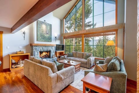 - Open-concept living room with soaring windows and forest views  
- Stone fireplace adds warmth to this bright inviting space  
- Perfect spot for cozy evenings and shared mountain moments  
