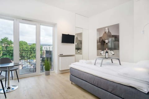 A spacious living room with a comfortable sofa, a TV, and a wardrobe, featuring large doors that open to a private balcony with outdoor views.