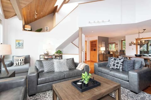 - Bright open-concept living room with vaulted ceilings and modern mountain decor  
- Plush seating around the stone fireplace for relaxing après-ski moments  
- Large windows invite natural light and showcase serene alpine scenery  
