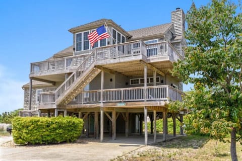 A distinctive coastal property featuring multi-level decks and classic shingled architecture, proudly displaying its beachside character beneath a bright blue sky.