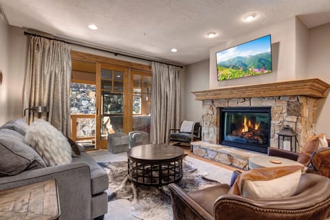 Cozy up in your elegant living room featuring a stone fireplace, plush seating, and mountain views through floor-to-ceiling windows.