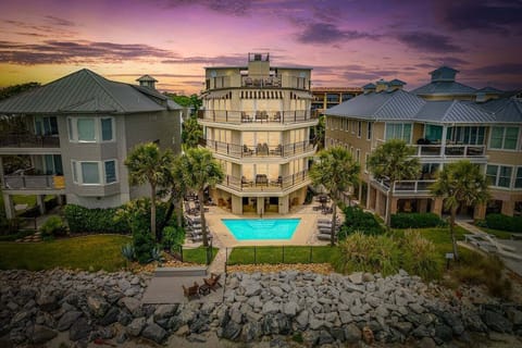 Multi-story beachfront property at sunset with pool and palms