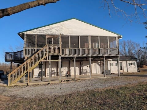Pond-facing exterior of Pond View Loft at Timber Oaks. This elevated loft above the barn features a screened-in porch, open-air deck, and private staircase — all overlooking the peaceful fishing pond and surrounding countryside.