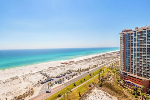 Pristine white sand beach stretches endlessly along turquoise waters, with nearby high-rise buildings offering convenient beachfront access.