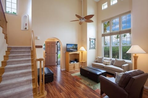 Living room with high ceilings, tall windows. Warm wood floors and ceiling fan add to the atmosphere