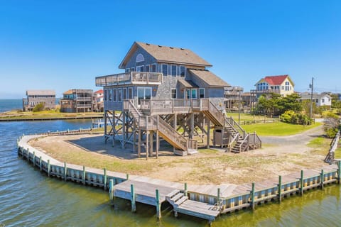 A coastal property elevated on pilings with private dock and waterfront access, surrounded by neighboring beach homes and open water views.
