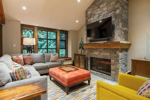 - Cozy living room with stone fireplace and forest views through large windows  
- Plush seating and vibrant accents create a warm, inviting mountain retreat  
- Perfect spot to relax after exploring trails or nearby attractions  

