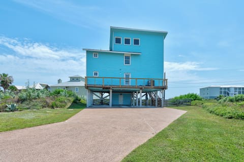 Striking beach house on stilts with covered parking below, surrounded by coastal landscape under a beautiful sky.