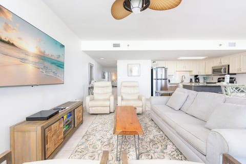 Bright living area featuring a comfortable gray sofa with queen sleeper, two recliners, and a view into the kitchen