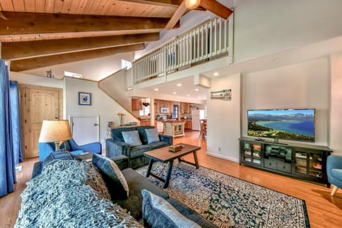 Vaulted ceiling with exposed wooden beams overlooks a living area featuring blue couches and a patterned rug.
