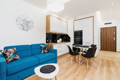 A bright living room with a teal sofa, a small white coffee table, and modern decor. The wooden floor adds warmth to the space.