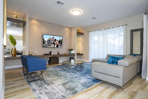 Neutral-tone leather sectional and blue armchairs surround a metal-framed glass coffee table on a patterned rug.